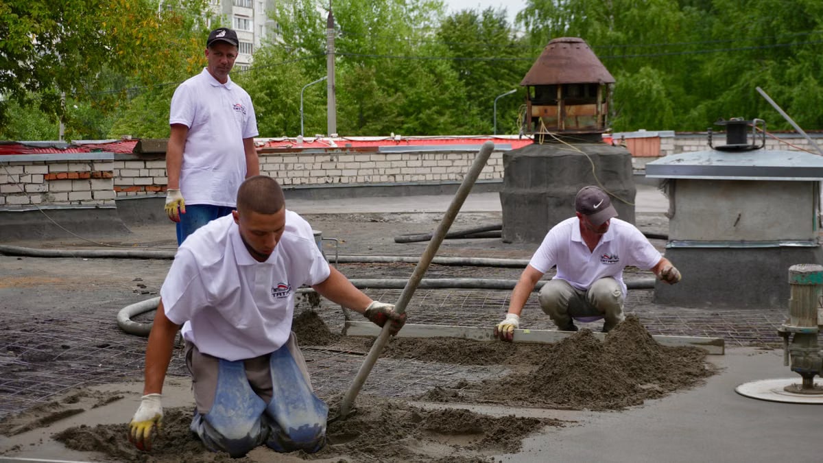 Three workers troweling and leveling cement on a rooftop construction project.